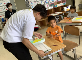 折り紙を先生にに見せる男の子